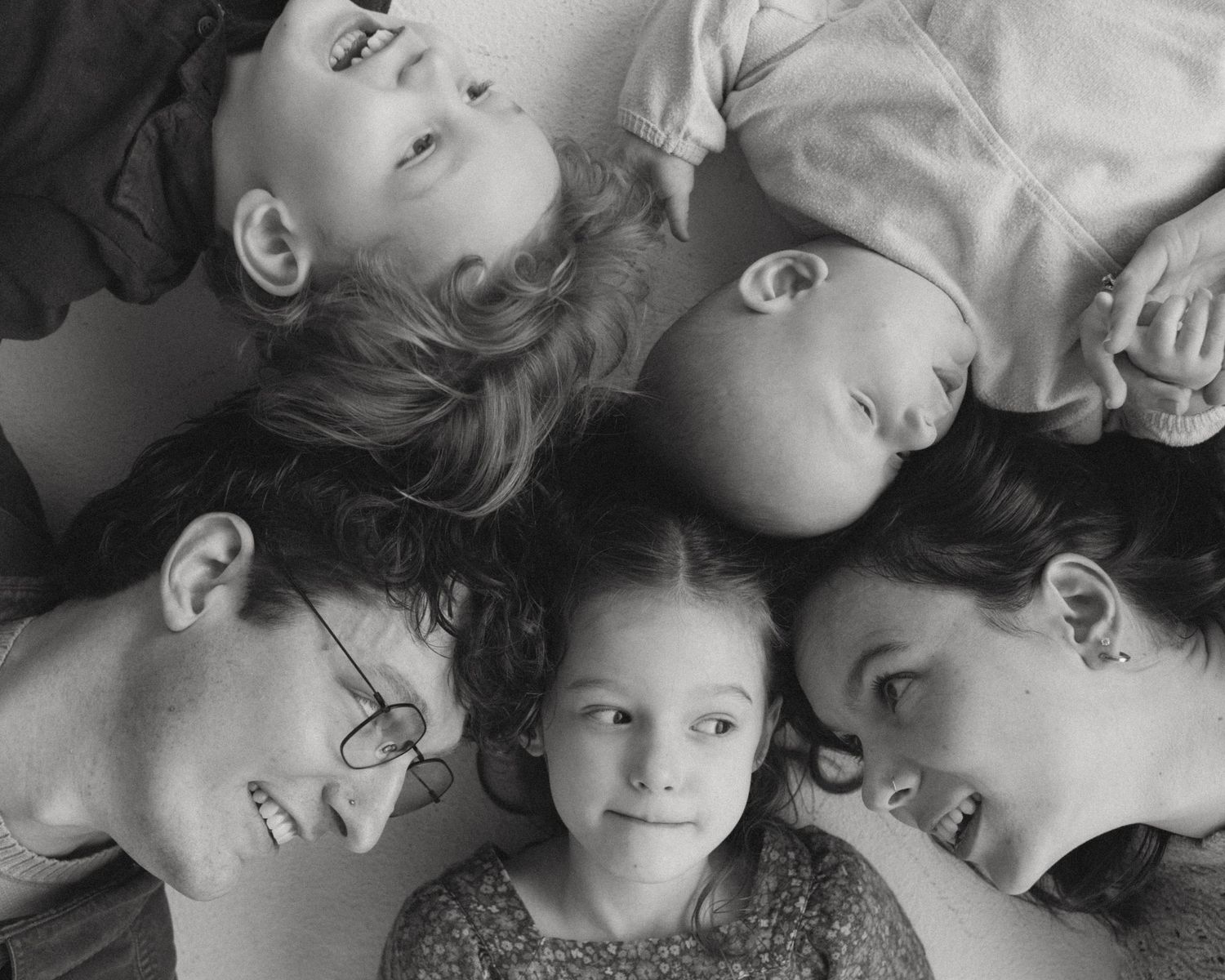 Black and white portrait of family members lying down in a circle formation with their heads together.