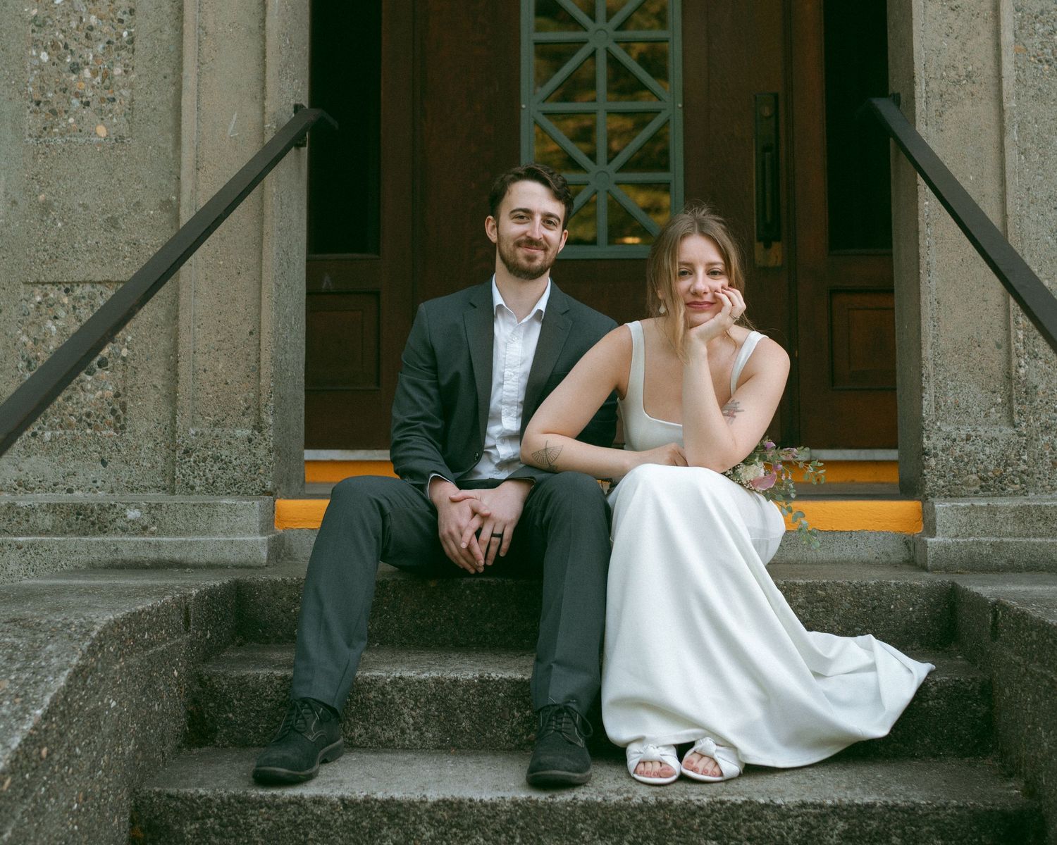 A happy couple sits together on stone steps outside a historic church building.