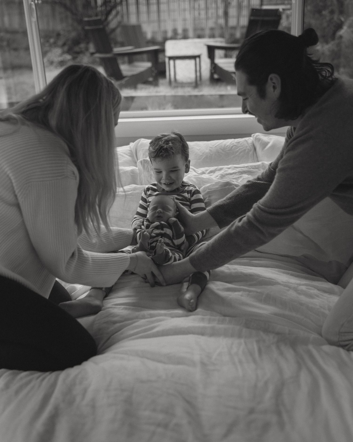 A black and white photo series showing tender moments between a parent and baby on a bed.