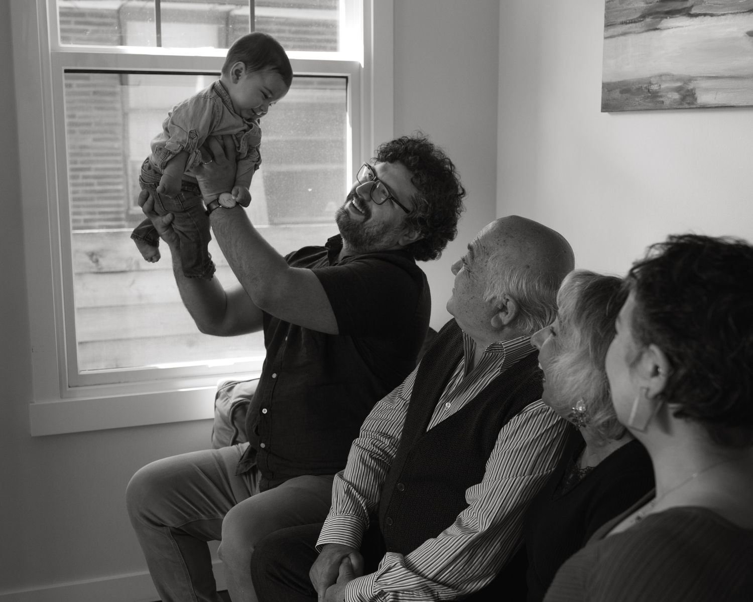 Multi-generational family gathering by window in black and white photograph.