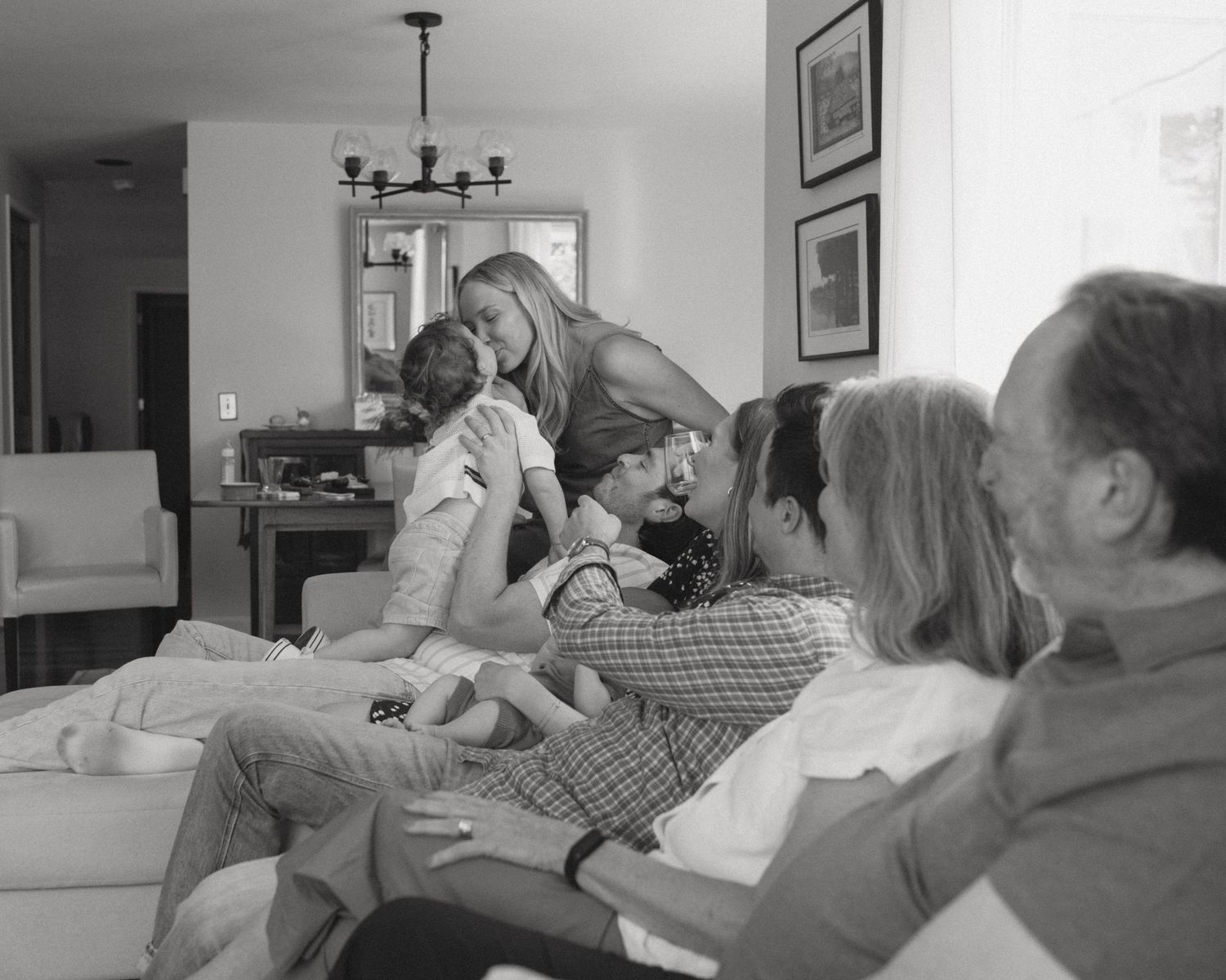 A casual family gathering scene in a living room with multiple generations relaxing together.