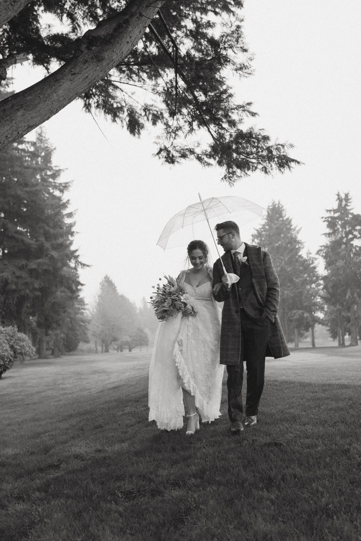 Misty black and white photo of people with umbrellas walking through a park landscape.