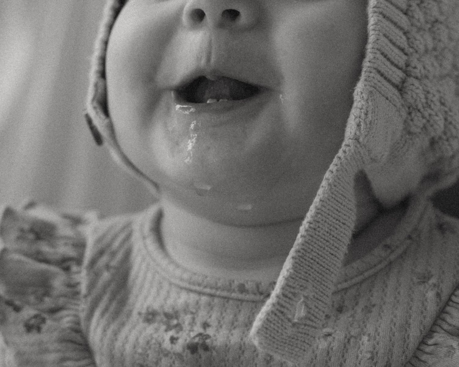 Adorable smiling baby wearing a knit bonnet hat with drool on chin in a classic black and white photo.