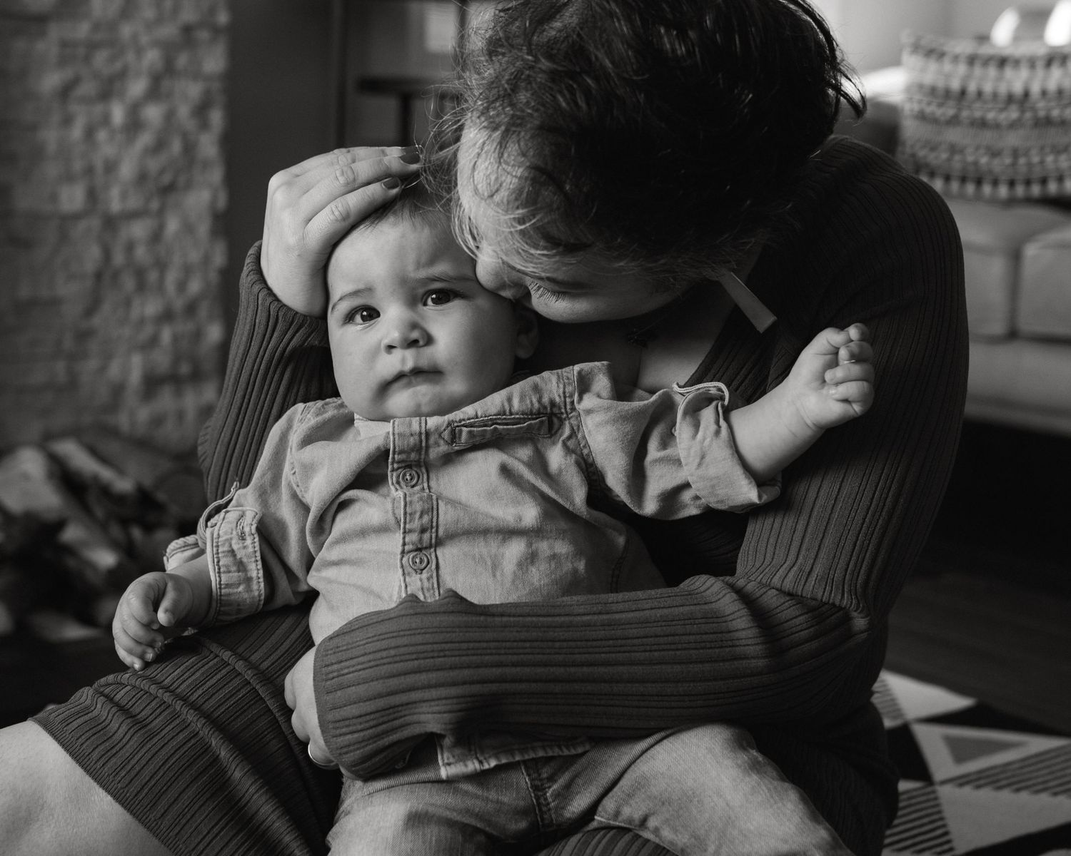 Black and white portrait of tender parent-child moment on patterned floor.