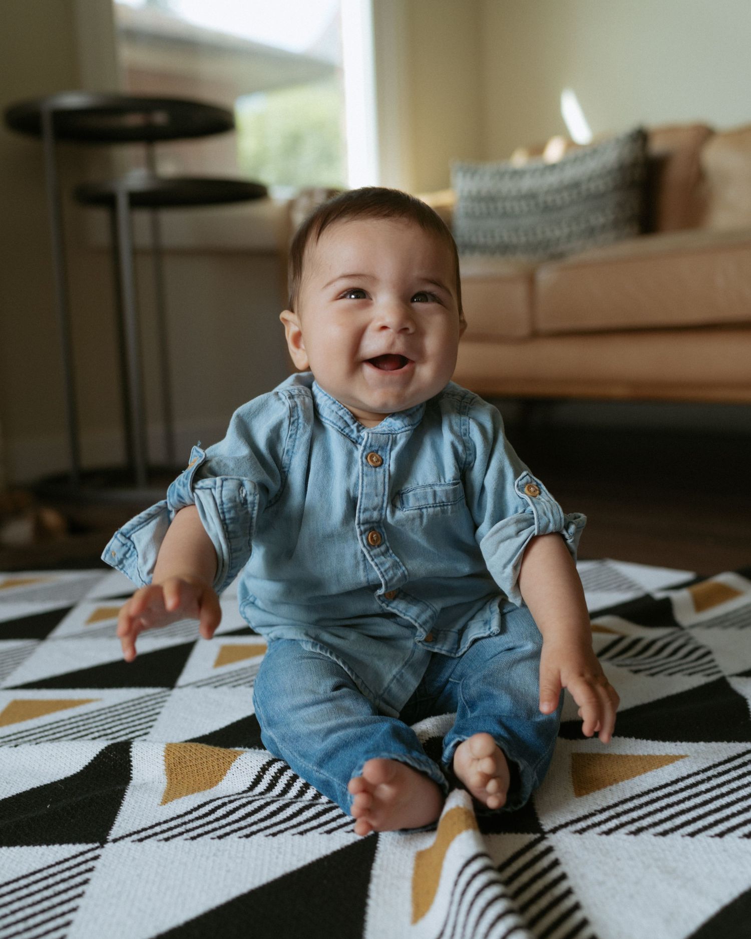 Smiling baby in denim outfit sits on geometric black and white rug.