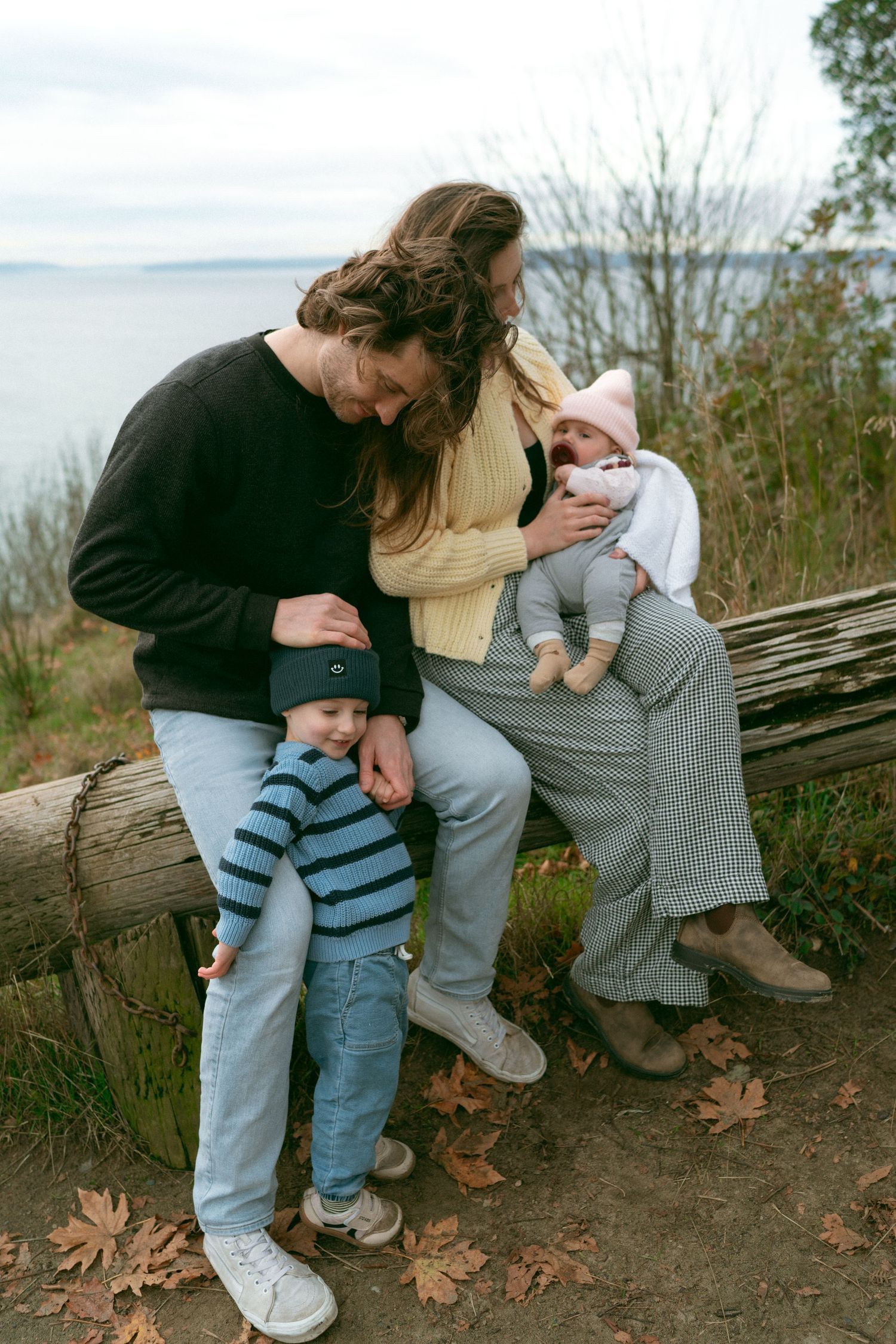 Family spending time together on a rustic log bench surrounded by fall foliage.