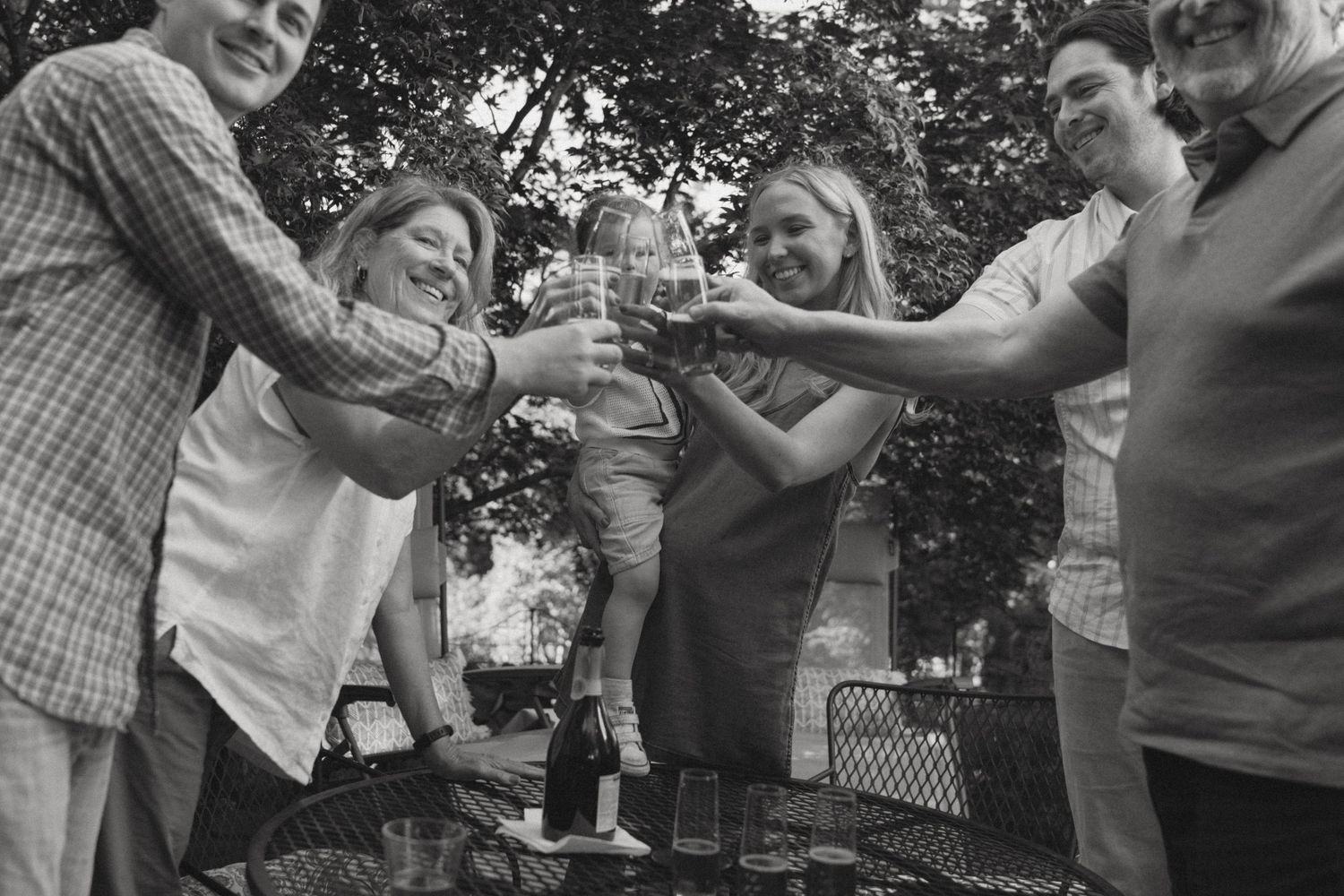 A black and white photo of family members toasting together at an outdoor gathering.