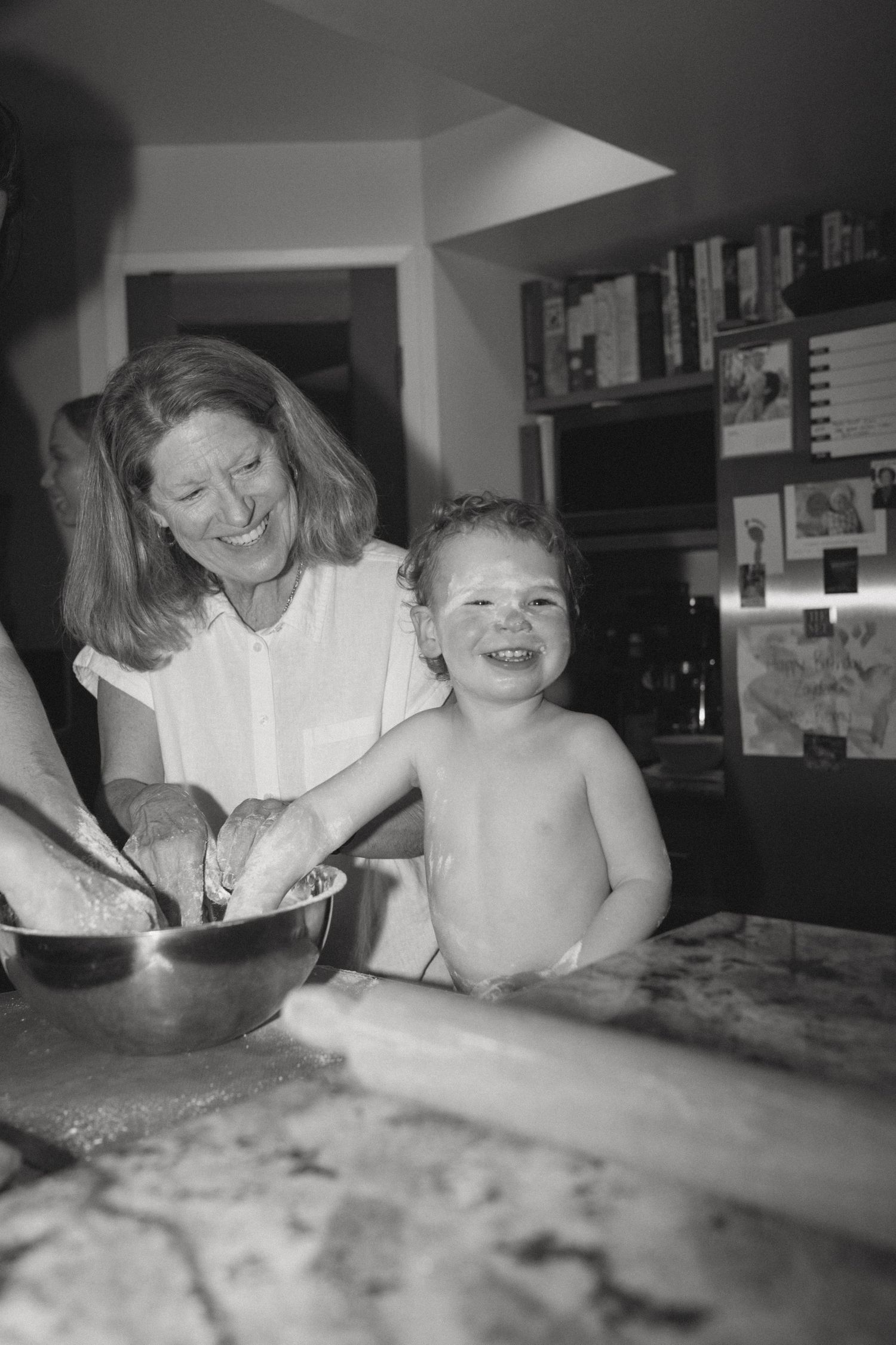 A joyful black and white photo of baking together in a kitchen with cookbooks in the background.