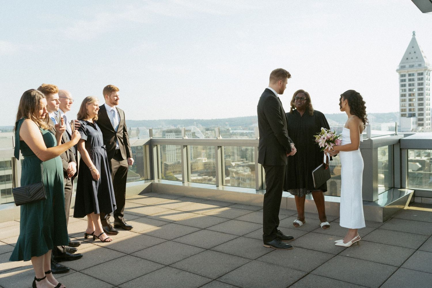Wedding guests gather on a rooftop terrace with urban skyline views.