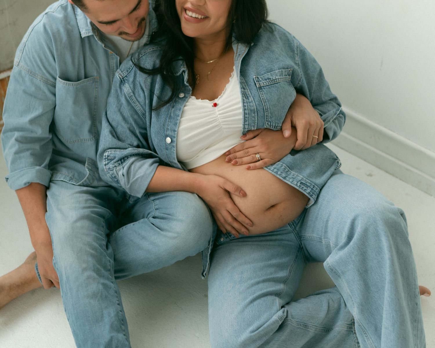 Couple in matching denim outfits sitting close together in bright interior setting.