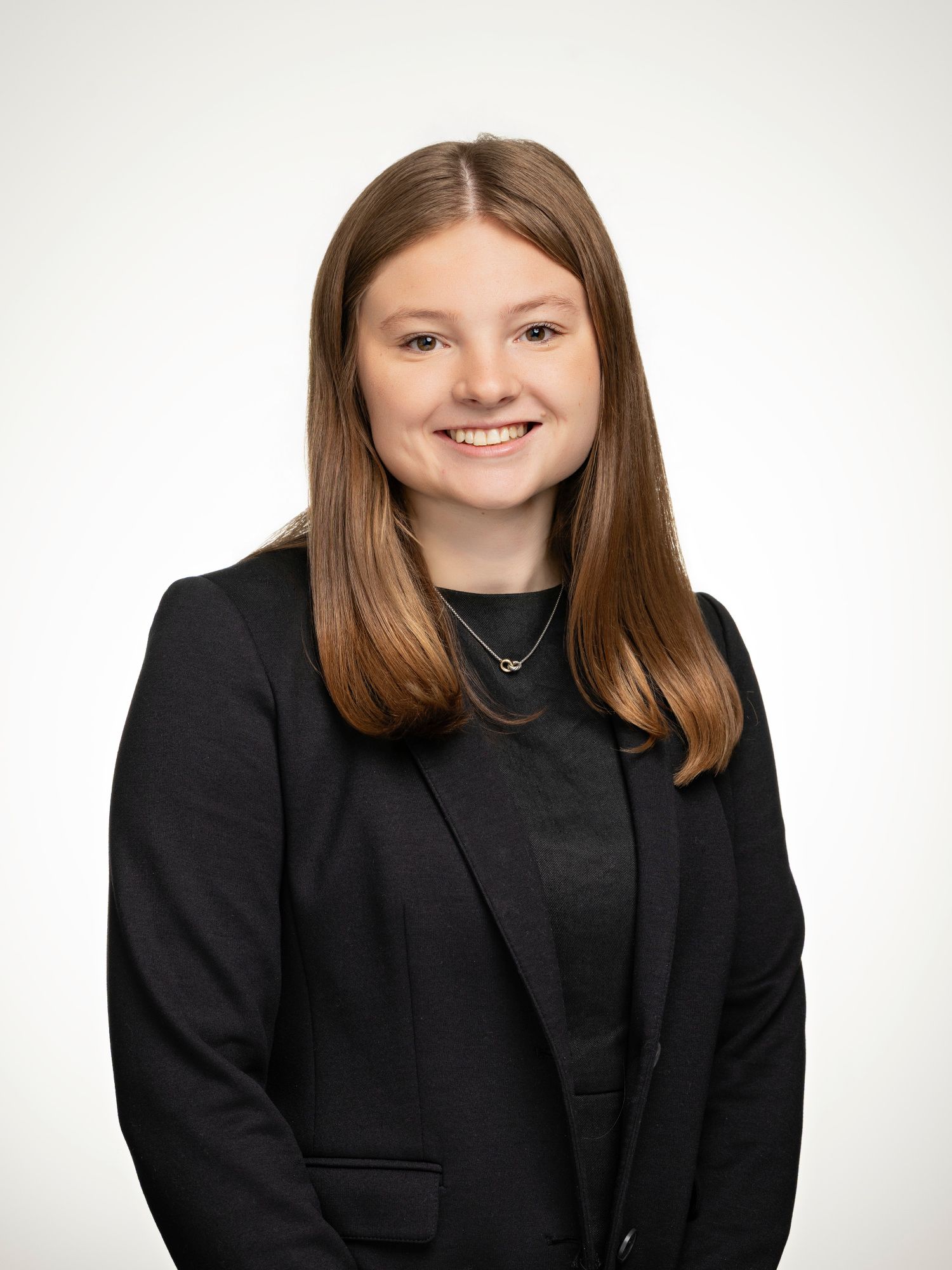 Young professional woman in black blazer smiling confidently against a neutral background in a formal headshot photo.