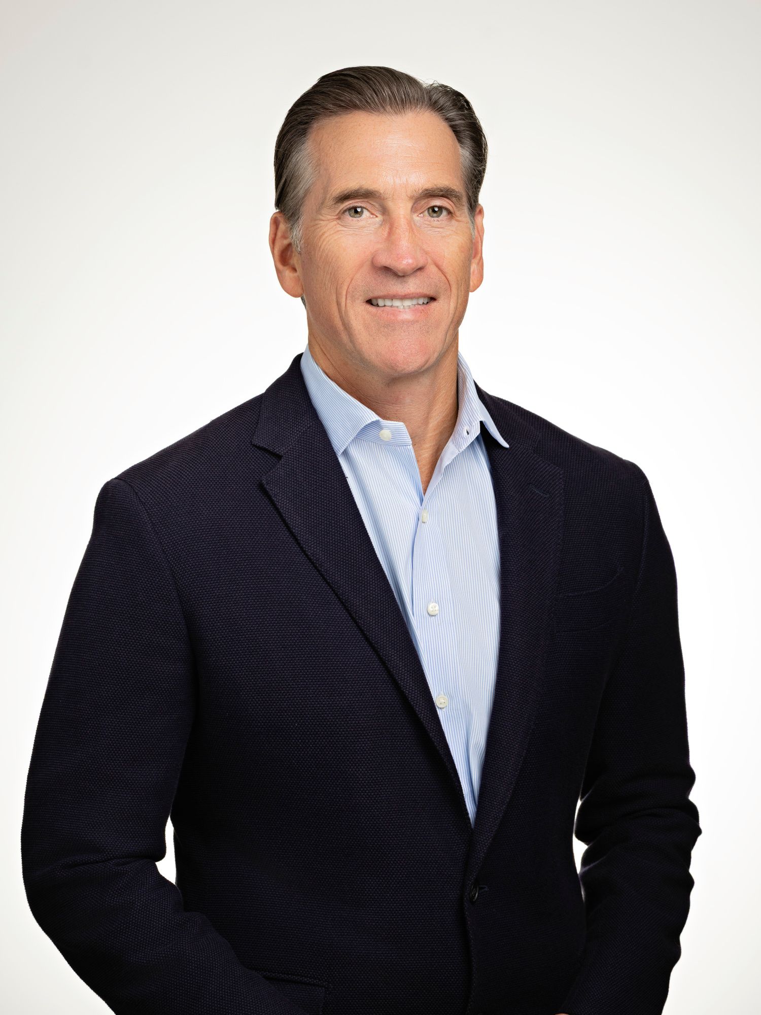 Professional headshot of a smiling middle-aged man in a navy blazer and light blue shirt against a white background.