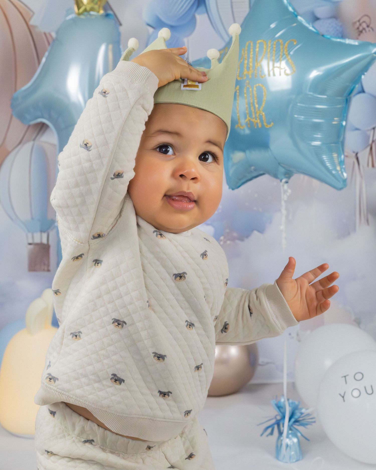Litet barn i ljus tröja leker med blå och vita stjärnformade ballonger under ett kalas.