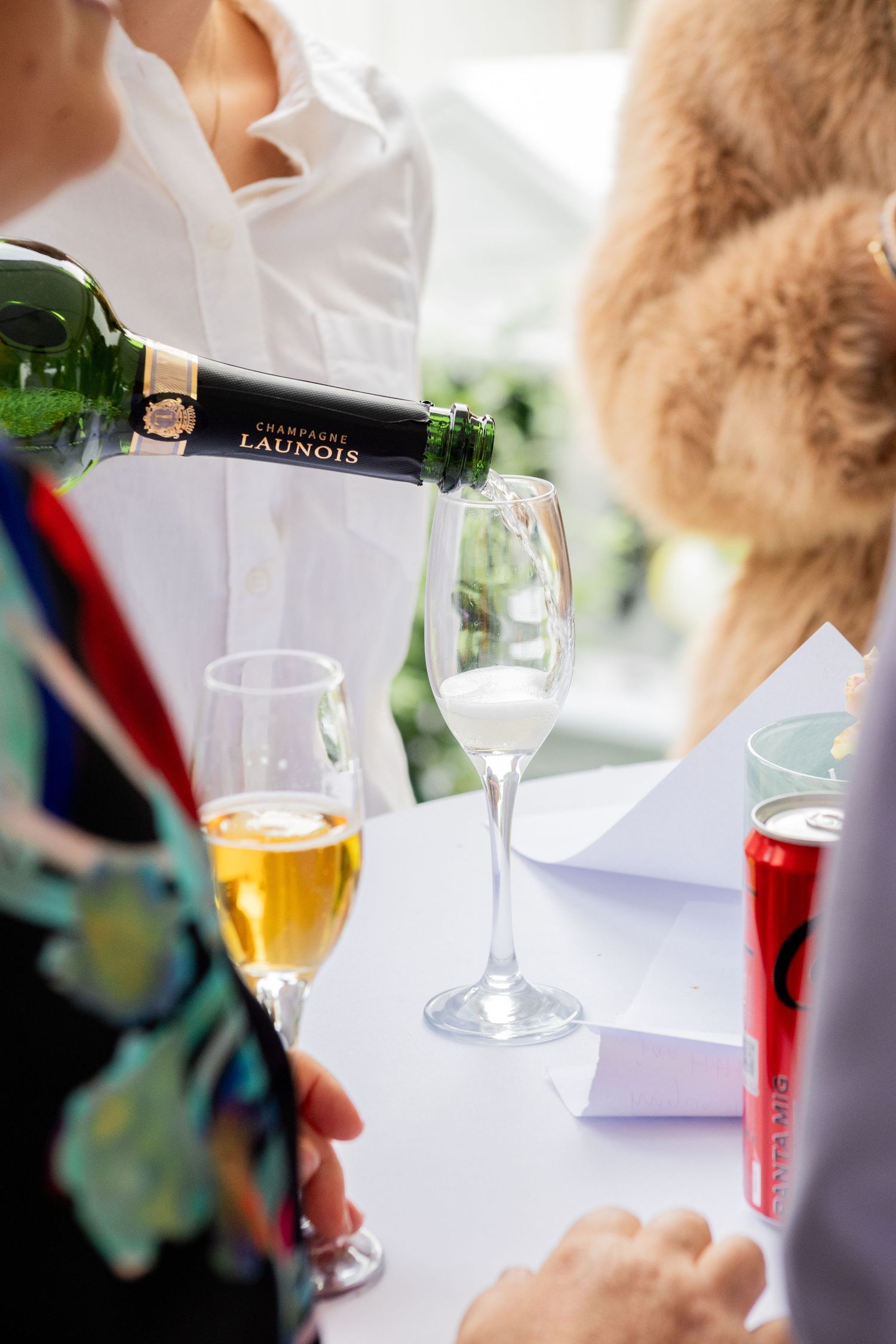 Champagne hälls upp i glas vid mingel, gäster står runt bord på bröllop eller företagsevent.