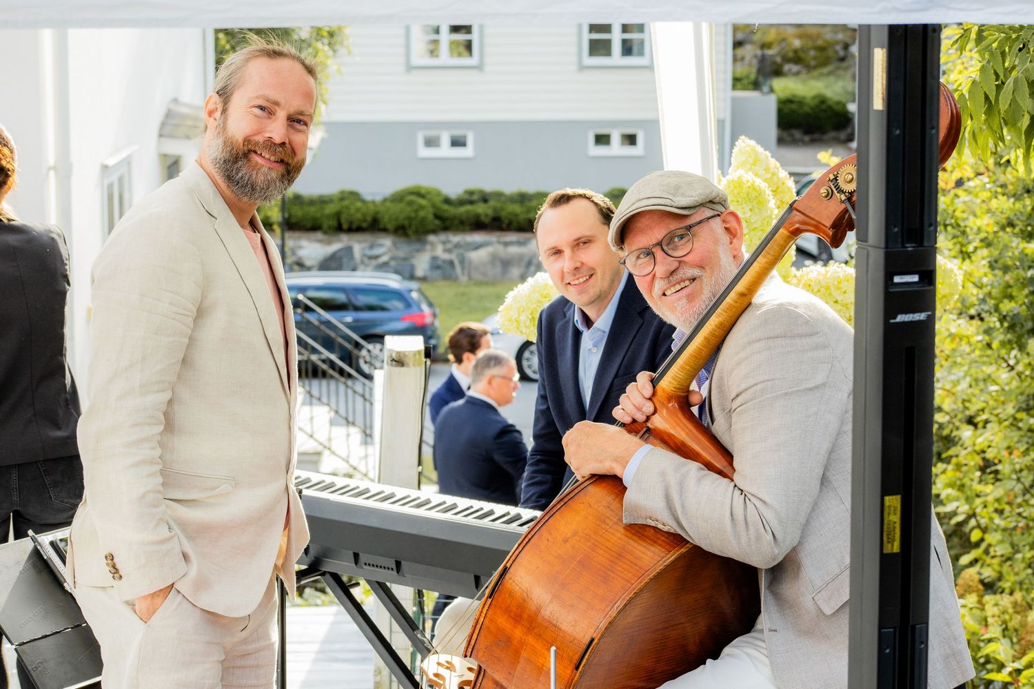 Musiker i ljusa kläder vid utomhusevent med kontrabas och keyboard, eventfotograf dokumenterar företagsevent.