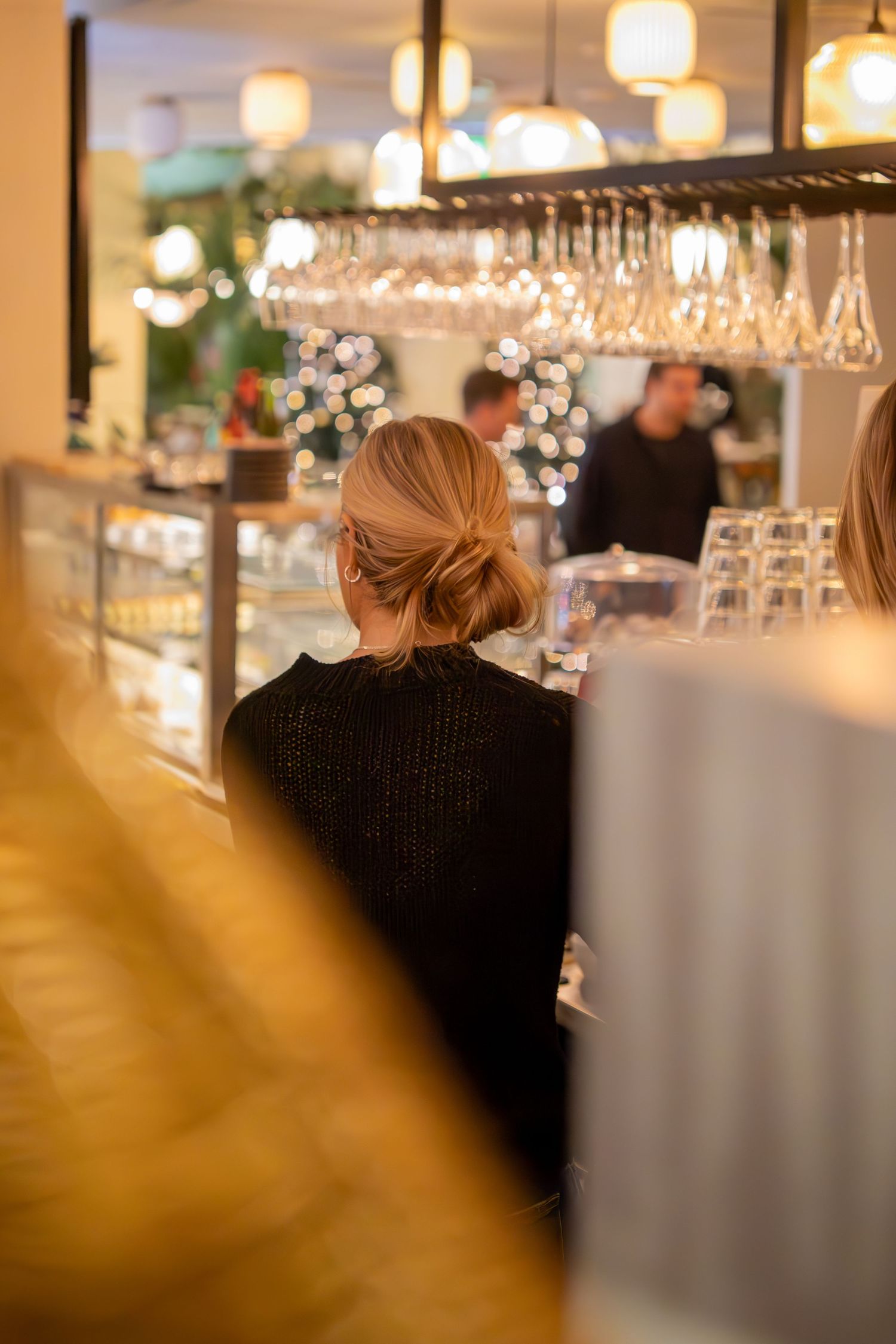 Person sitter vid bardisk med upphängda vinglas, restaurangmiljö dokumenterad av eventfotograf.