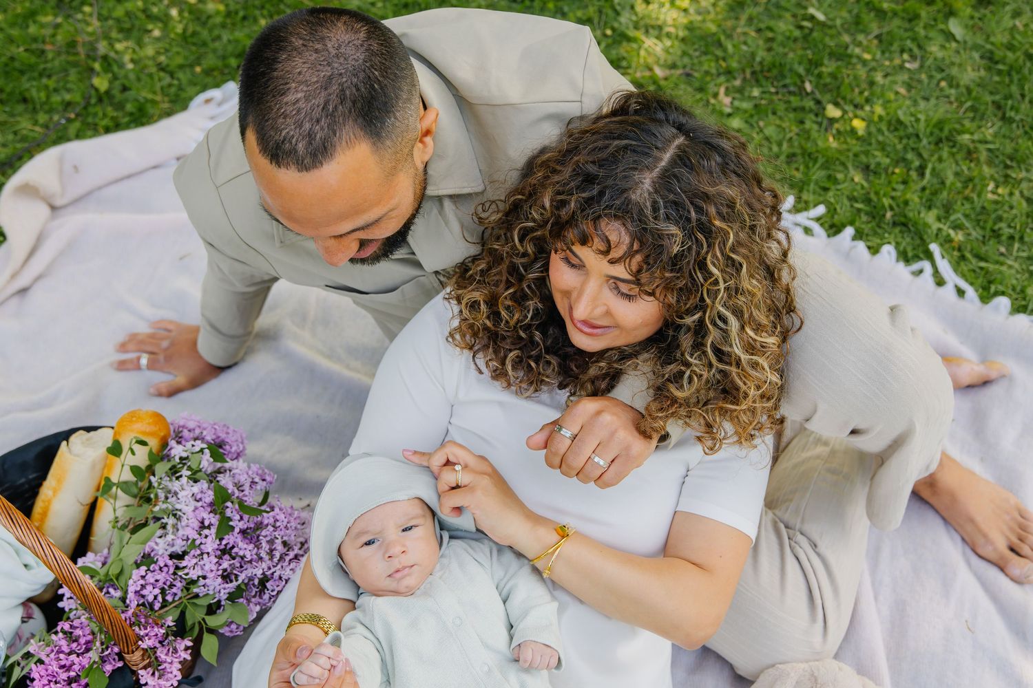 Familjefotografering utomhus med picknickfilt bland lila vildblommor i somrig natur.