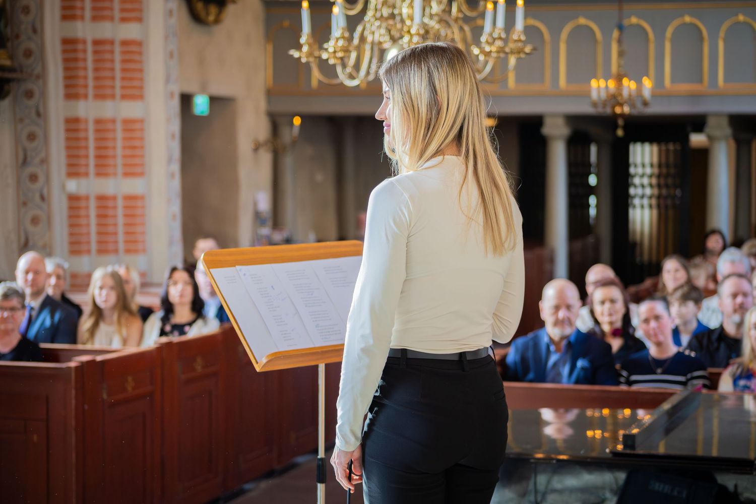 Person står vid talarstol framför församling under dopceremoni i kyrka, dokumentär dopfotografering.