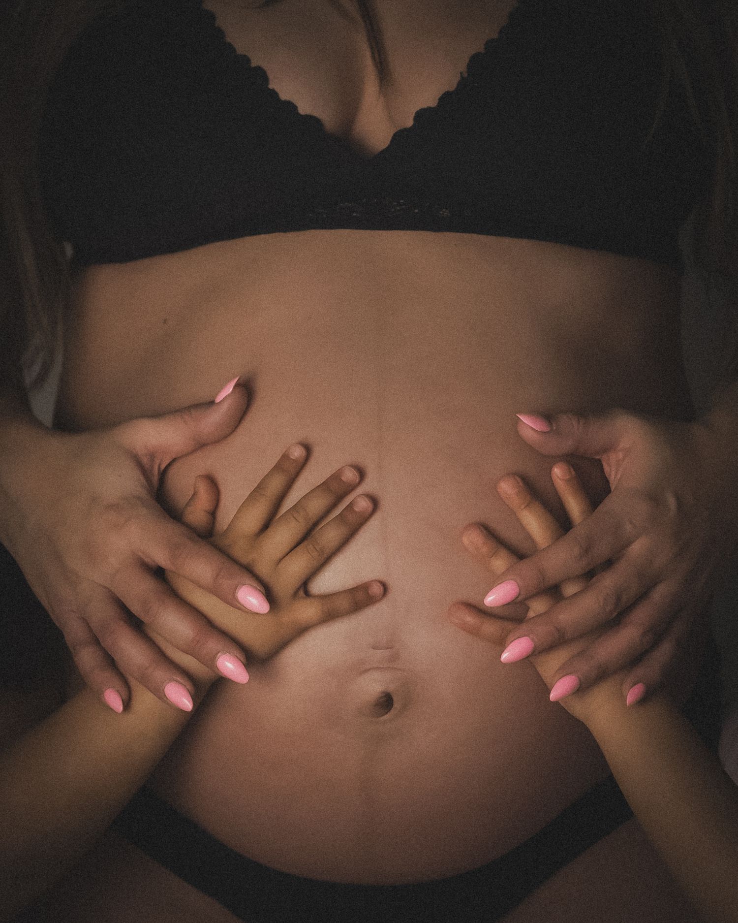 Närbild från konstnärlig gravidfotografering med små händer som håller om gravid mage.