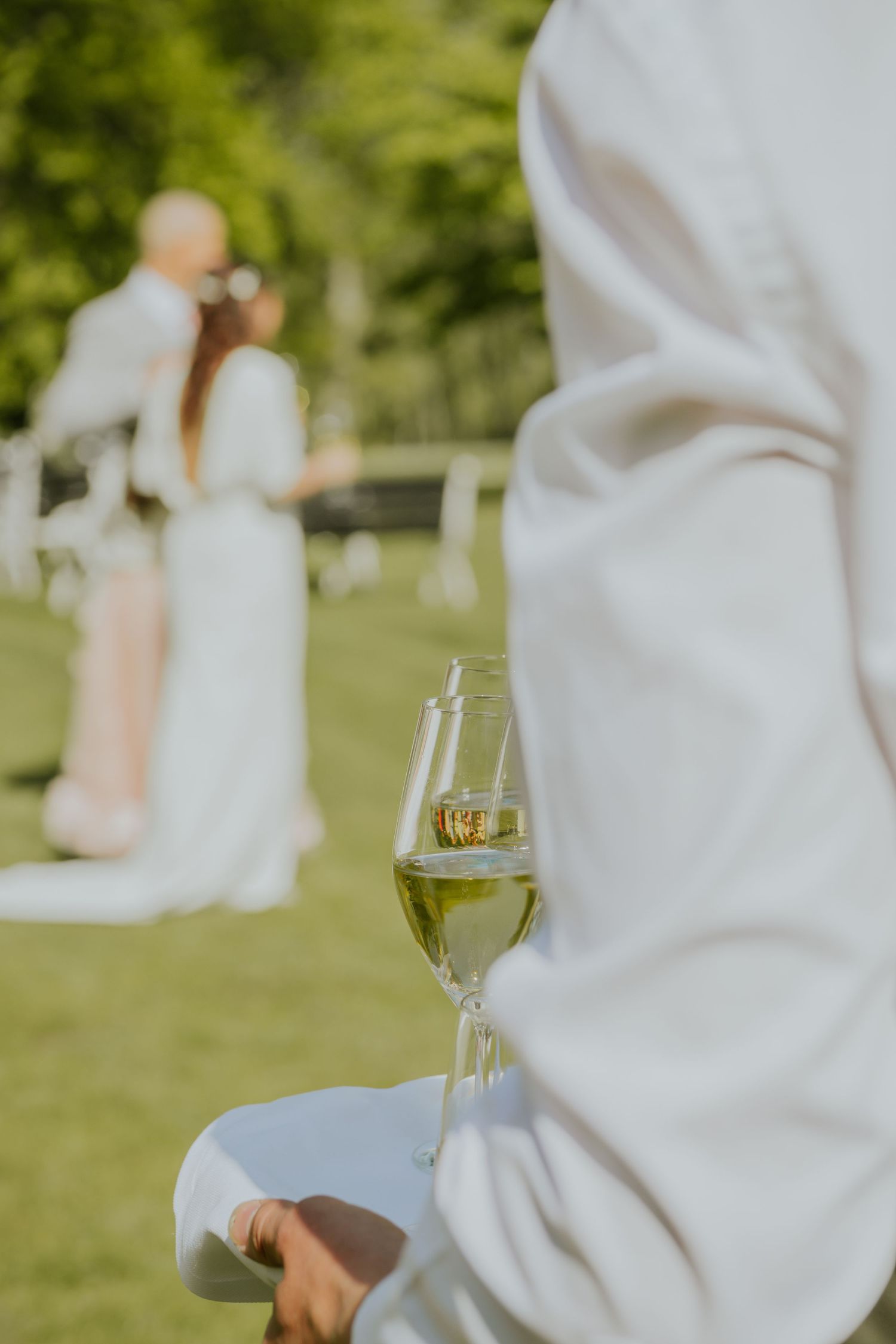 Champagneglas i förgrunden med brudpar i bakgrunden under bröllopsmingel i Stockholm, fångat av bröllopsfotograf i naturligt ljus.