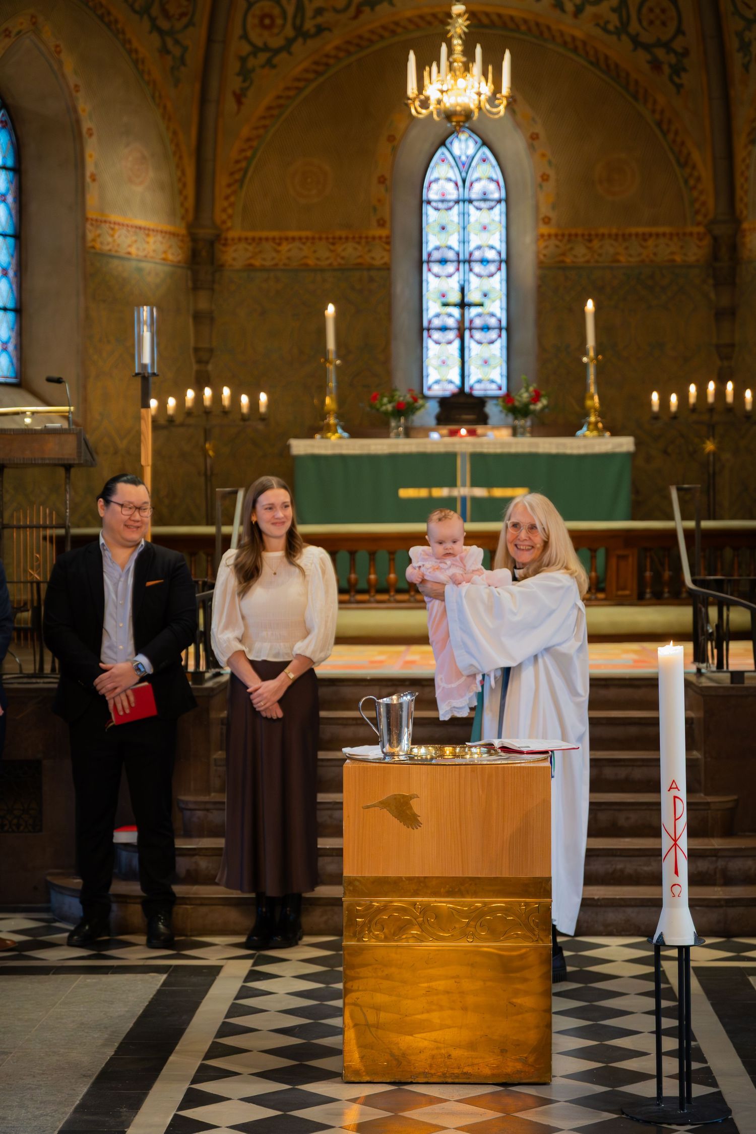Dopceremoni i kyrka där präst håller upp barnet vid dopfunten, fotograferat av dopfotograf i Stockholm.
