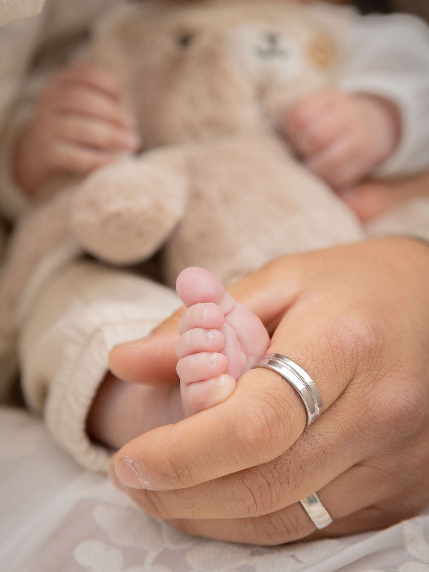 Nyfödds fot i kontakt med förälderns hand med vigselring under nyföddfotografering.