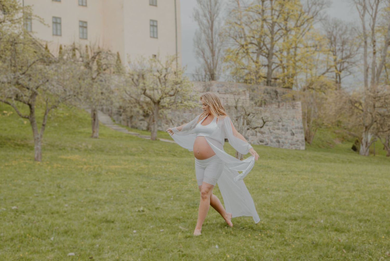 Gravid kvinna i flödande klänning under en romantisk gravidfotografering utomhus i Stockholm.