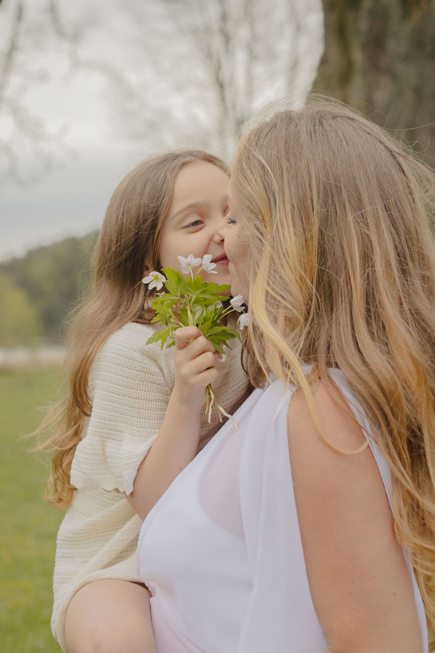 Liten flicka ger sin mamma vitsippor blommor under en varm och naturlig familjefotografering i Stockholm.