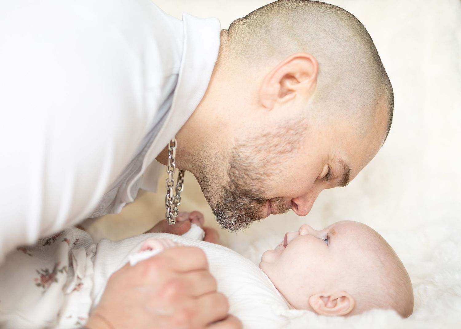 Pappa i vit skjorta lutar sig ner för att kyssa sovande bebis under familjefotografering.