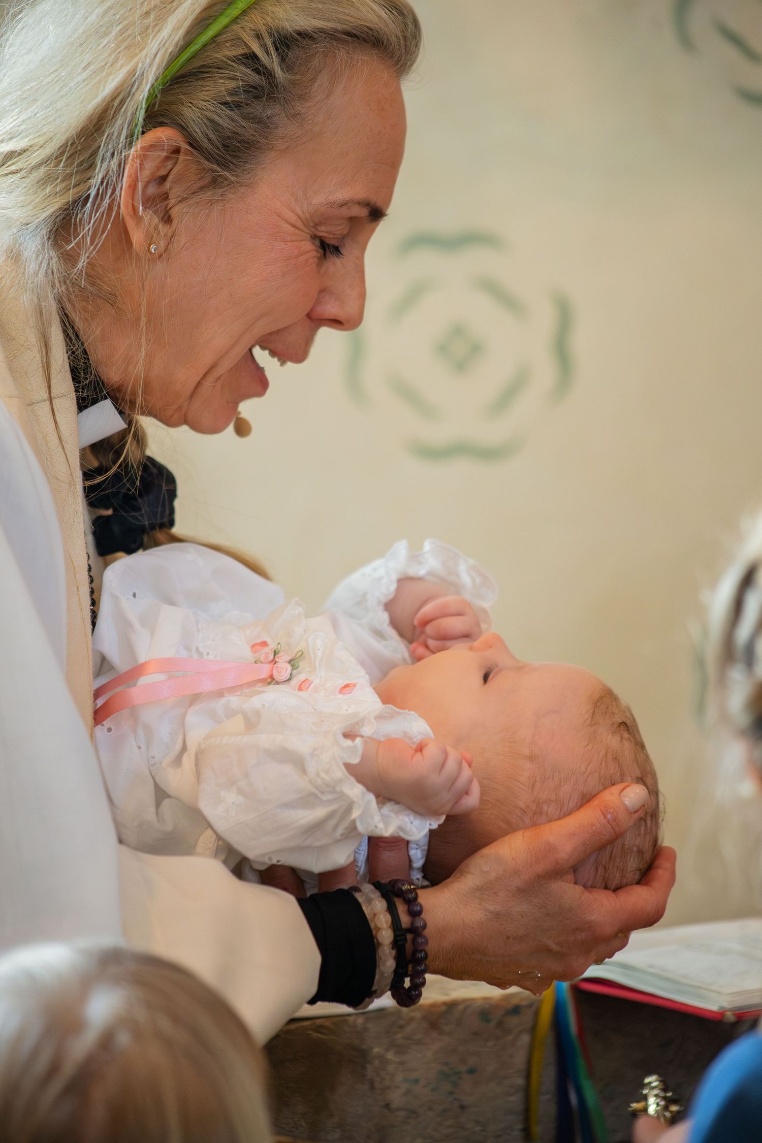 Präst håller bebis över dopfunt under dop i kyrka, närbild från dopfotografering.