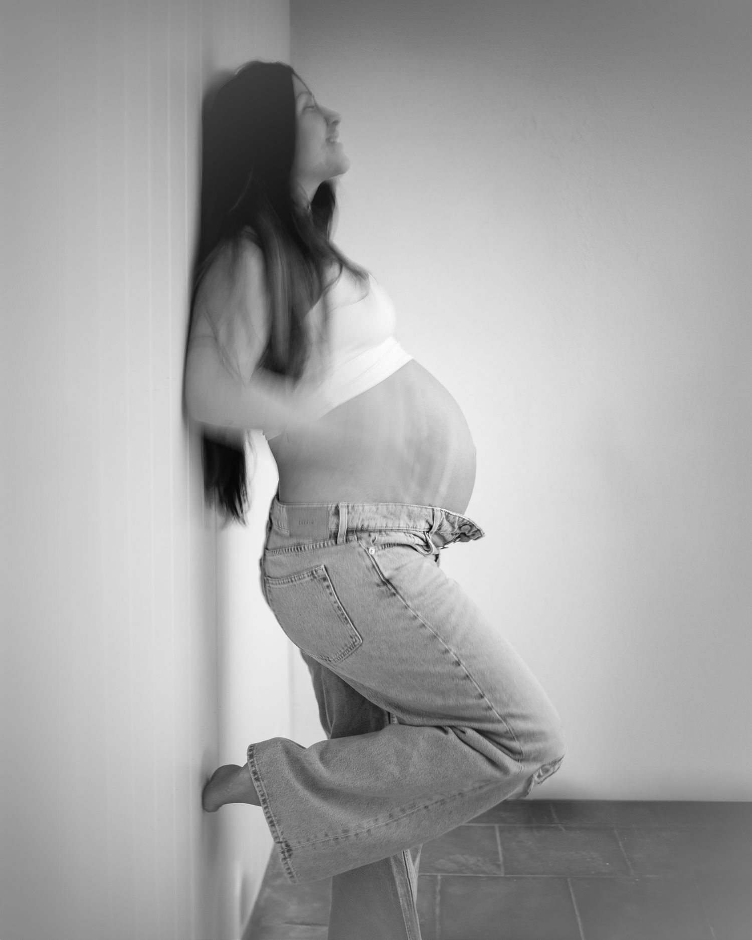 Svartvit gravidfotografering med profilposer mot vit vägg.