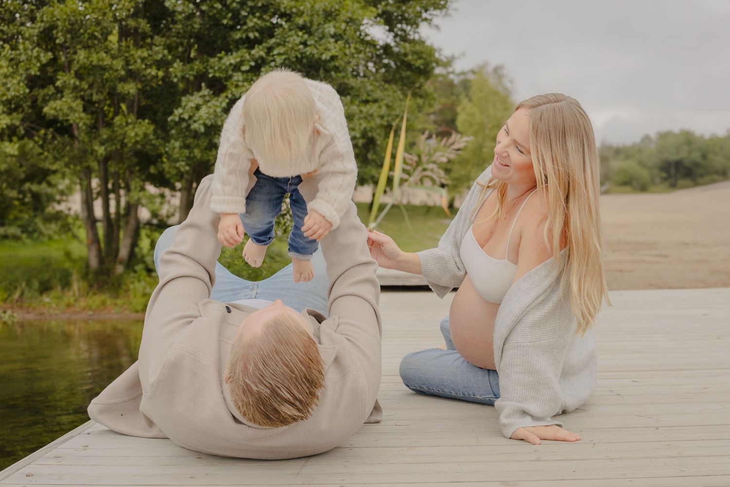 Gravid familj leker med sitt barn vid sjön under en naturlig familje- och gravidfotografering i Stockholm.