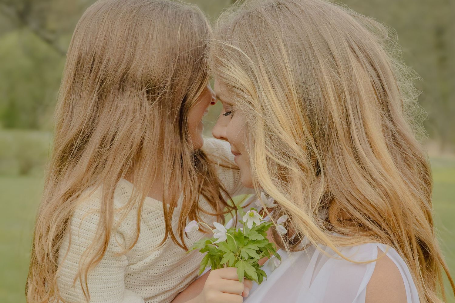 Mor och dotter står panna mot panna och håller en liten blomsterbukett under en familjefotografering i Stockholm