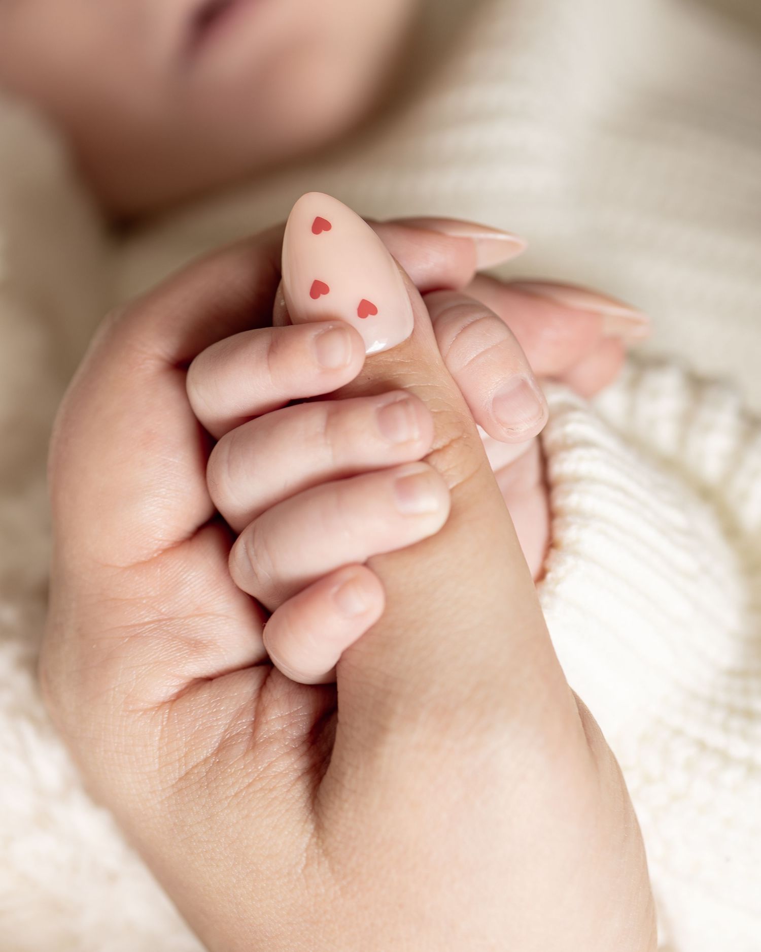 Närbild på nyfödds hand med hjärtdekoration som hålls av vuxen hand under nyföddfotografering.