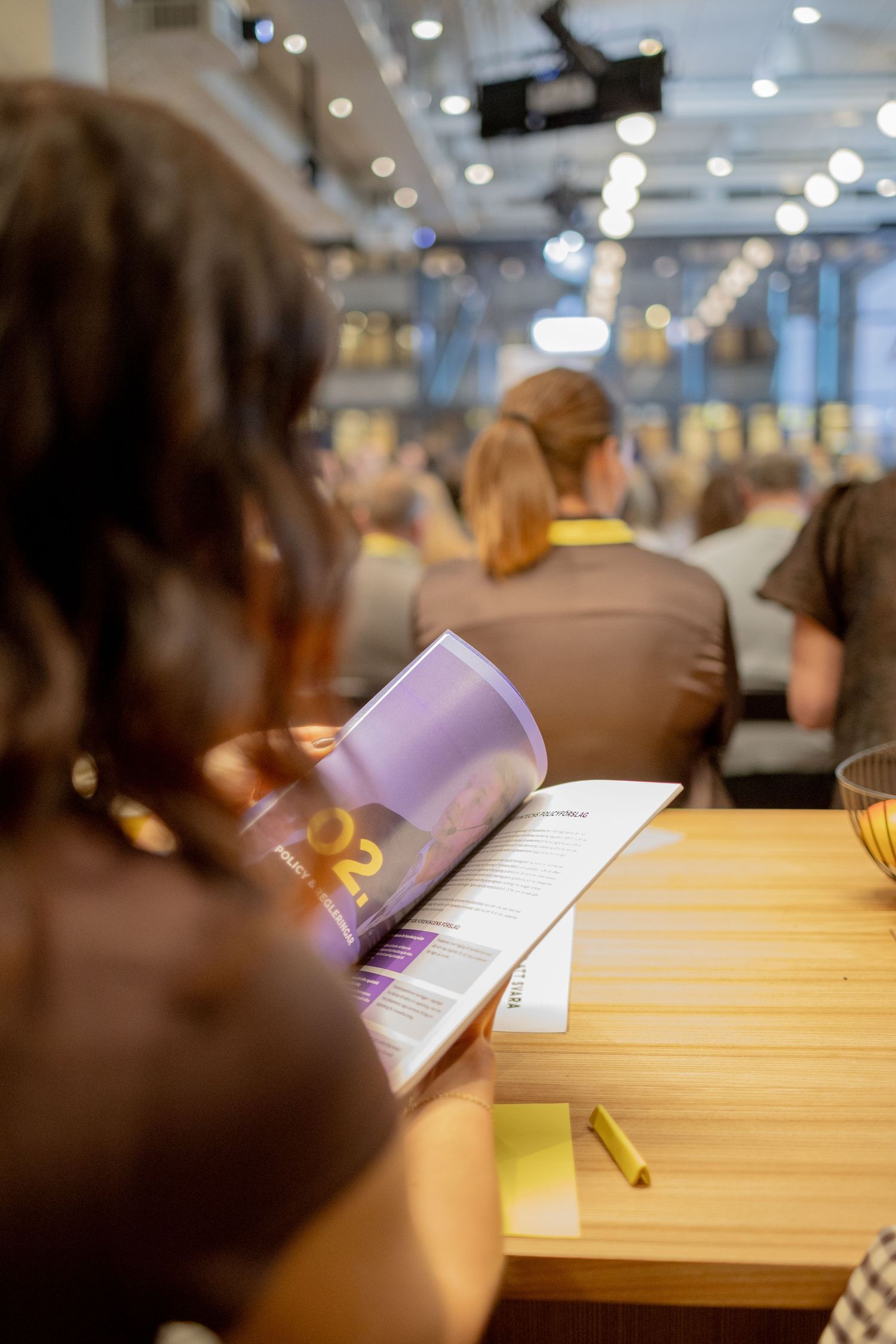 Deltagare sitter på konferens med program i handen, eventfotograf och företagsfotograf dokumenterar seminarium.