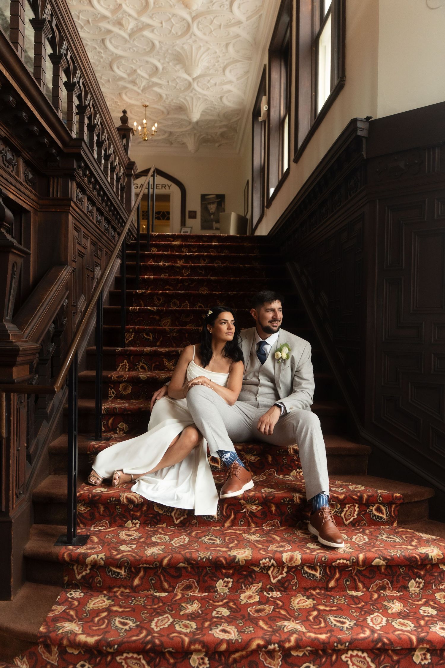 Wedding couple poses on ornate carpeted stairs in a vintage building interior. Branford House Uconn Connecticut Wedding venue Rhode Island