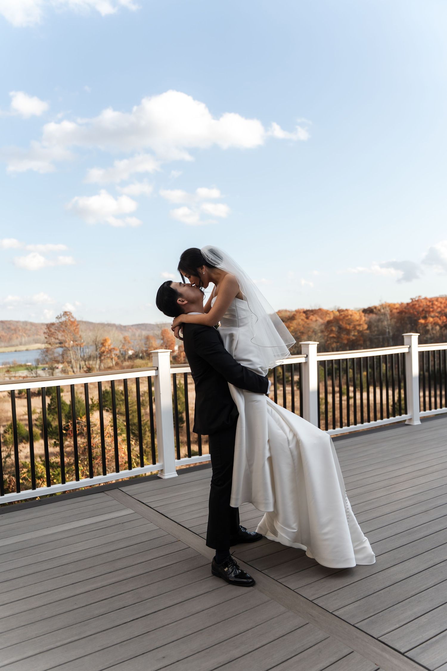 Romantic wedding couple dancing and dipping on an outdoor deck with autumn foliage in the background.