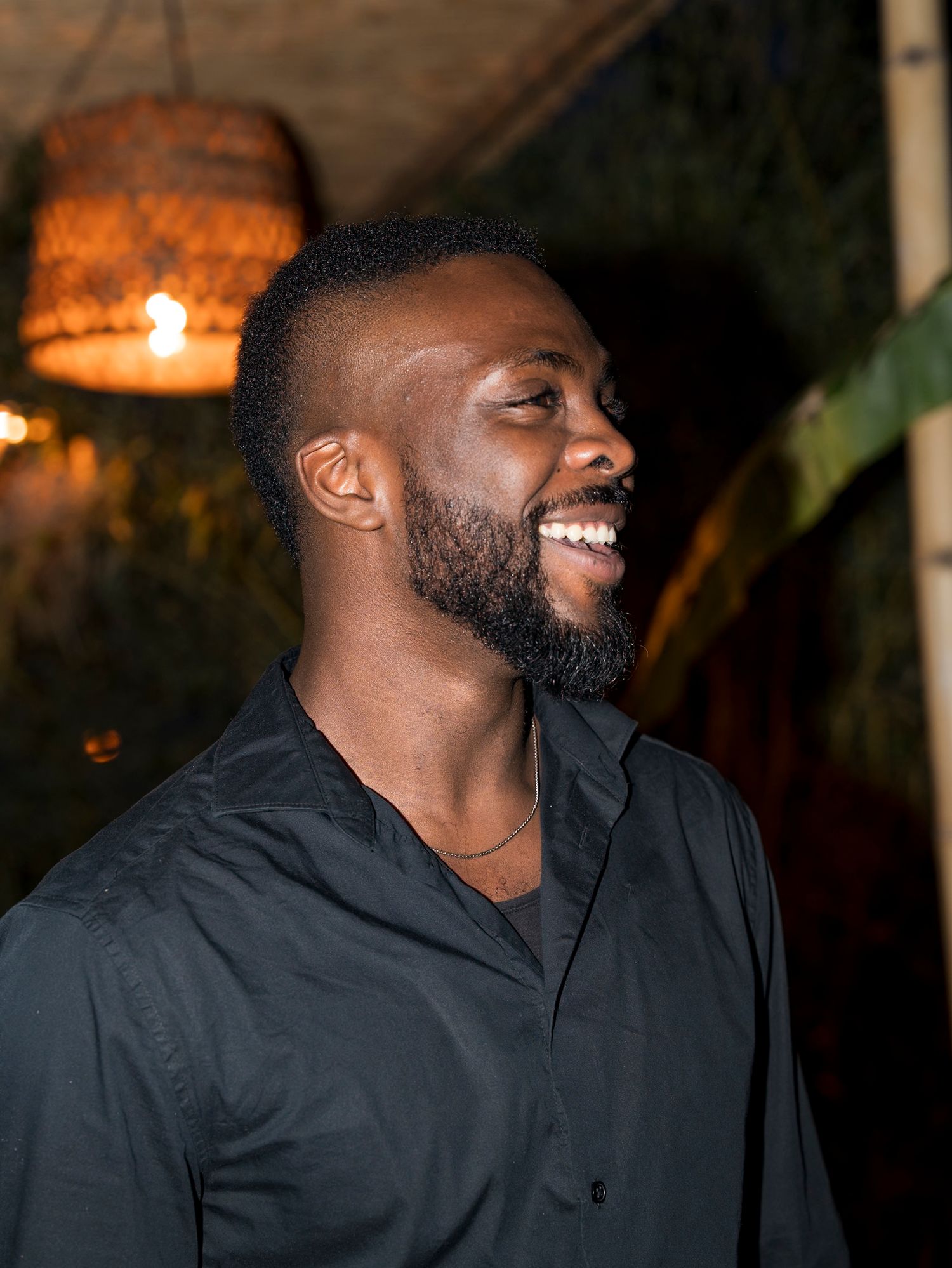 Portrait of a smiling man in black shirt with warm lighting and blurred background.