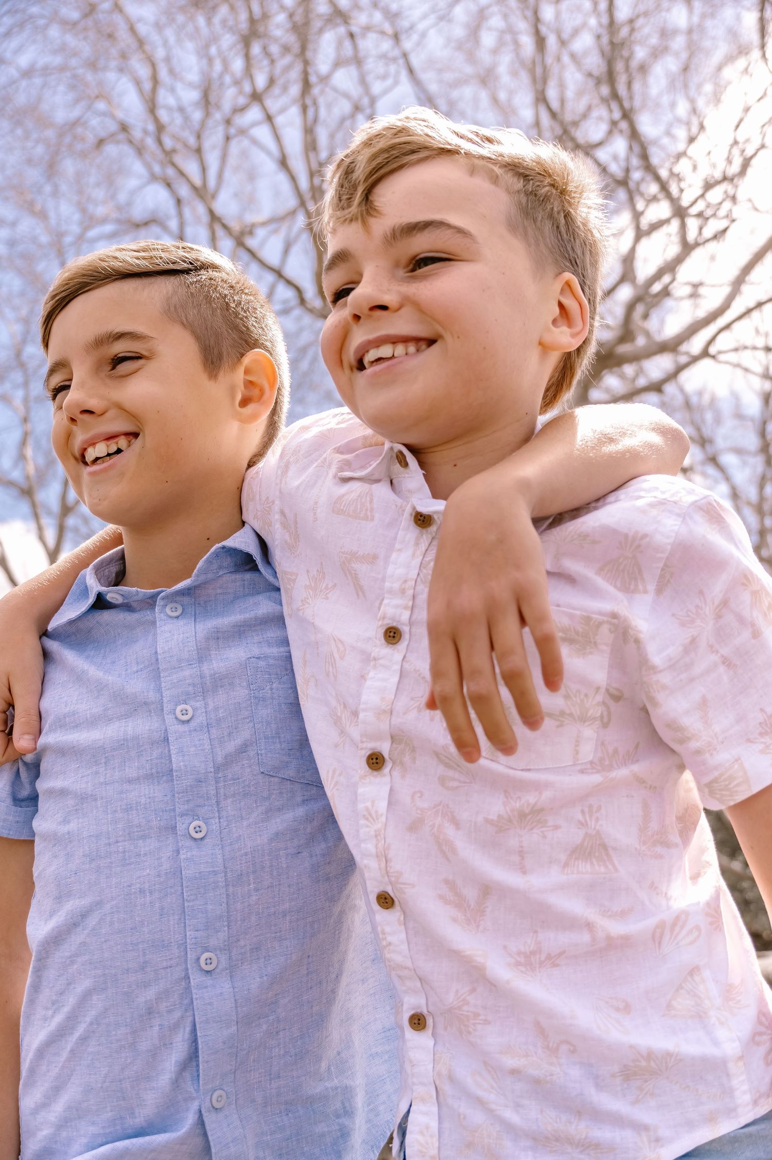 Two young boys laughing and embracing outdoors against a winter sky backdrop.