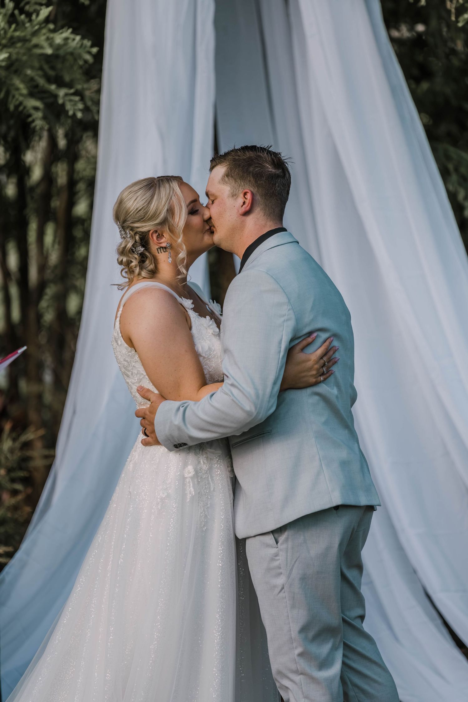 Wedding couple embracing in front of flowing white fabric backdrop.