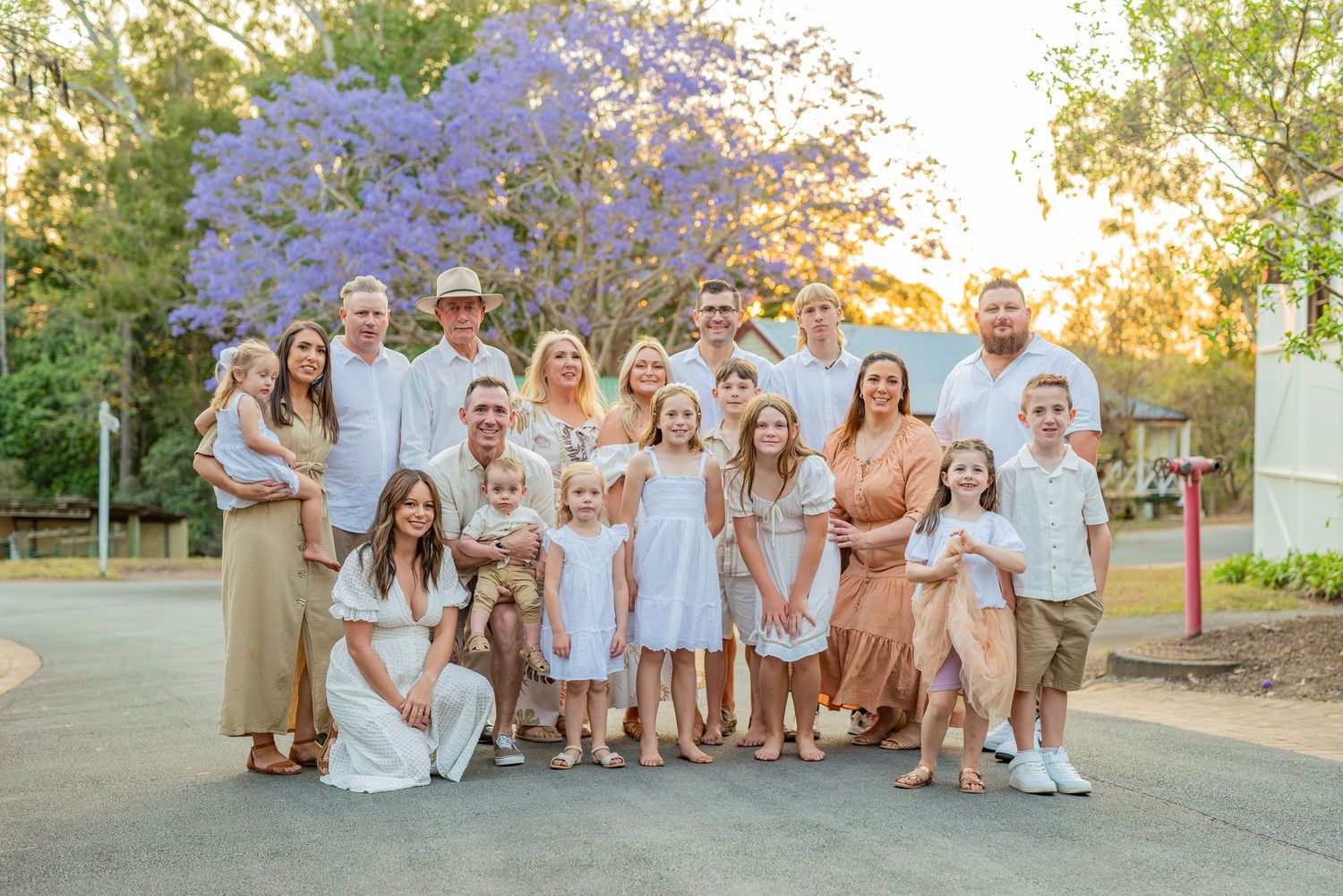 Extended family gathered outdoors for a portrait with blooming jacaranda tree in the background.