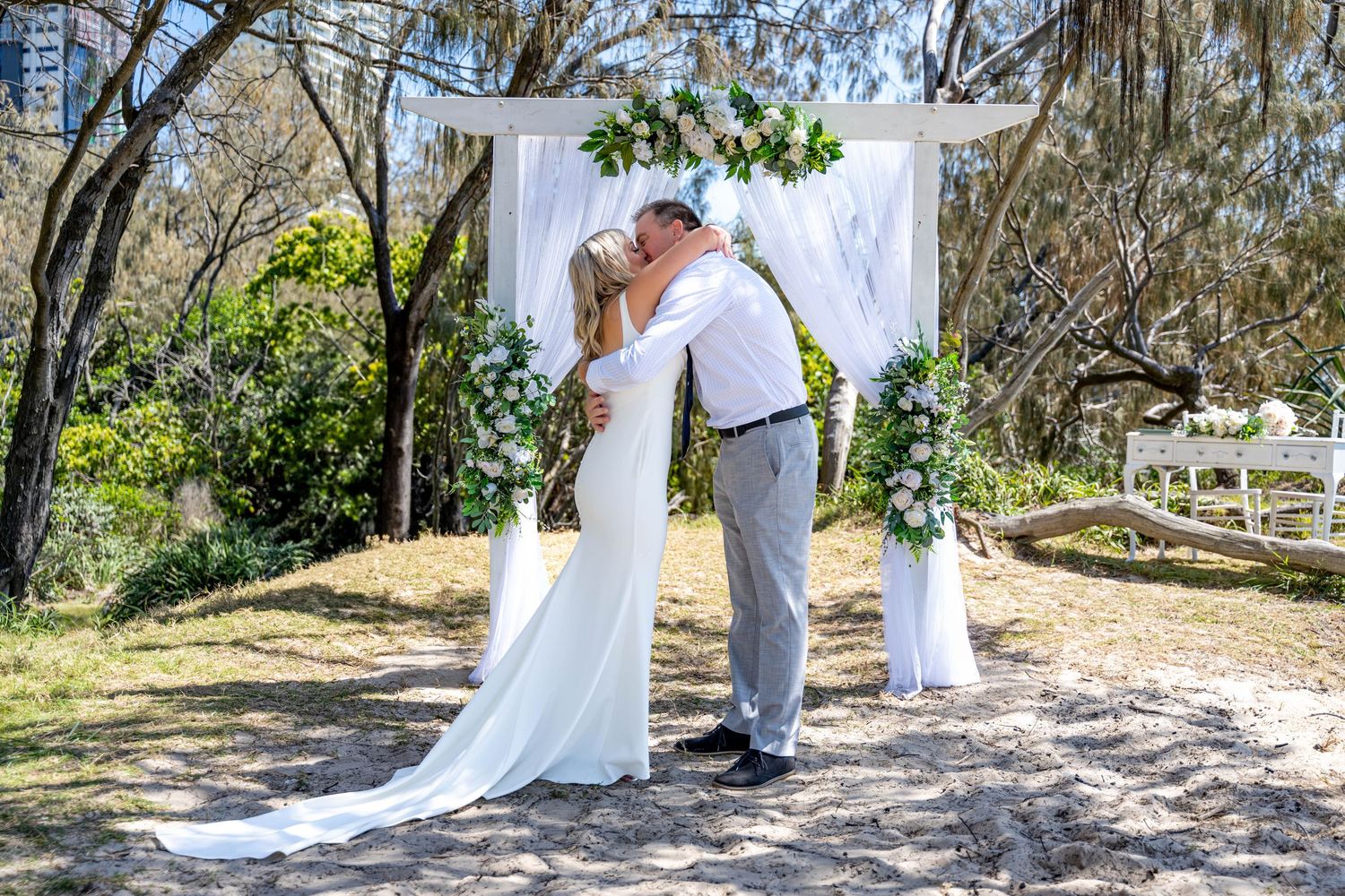 Wedding ceremony setup with white draping and natural tree backdrop in a rustic outdoor setting.