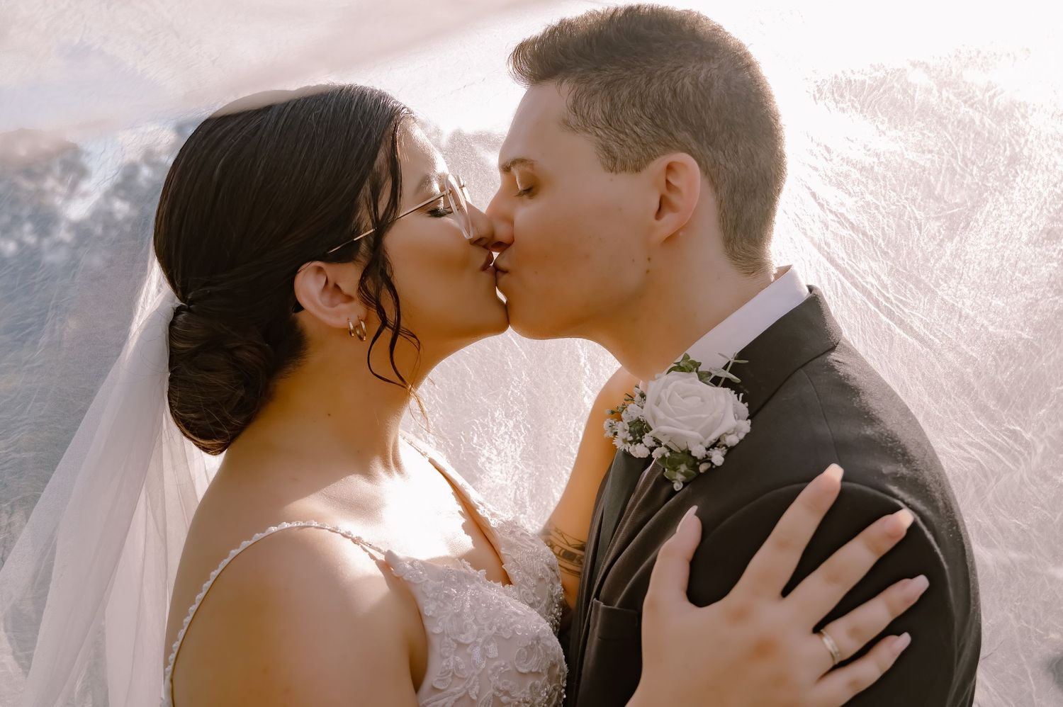 Silhouetted couple shares romantic kiss at sunset during outdoor wedding ceremony.