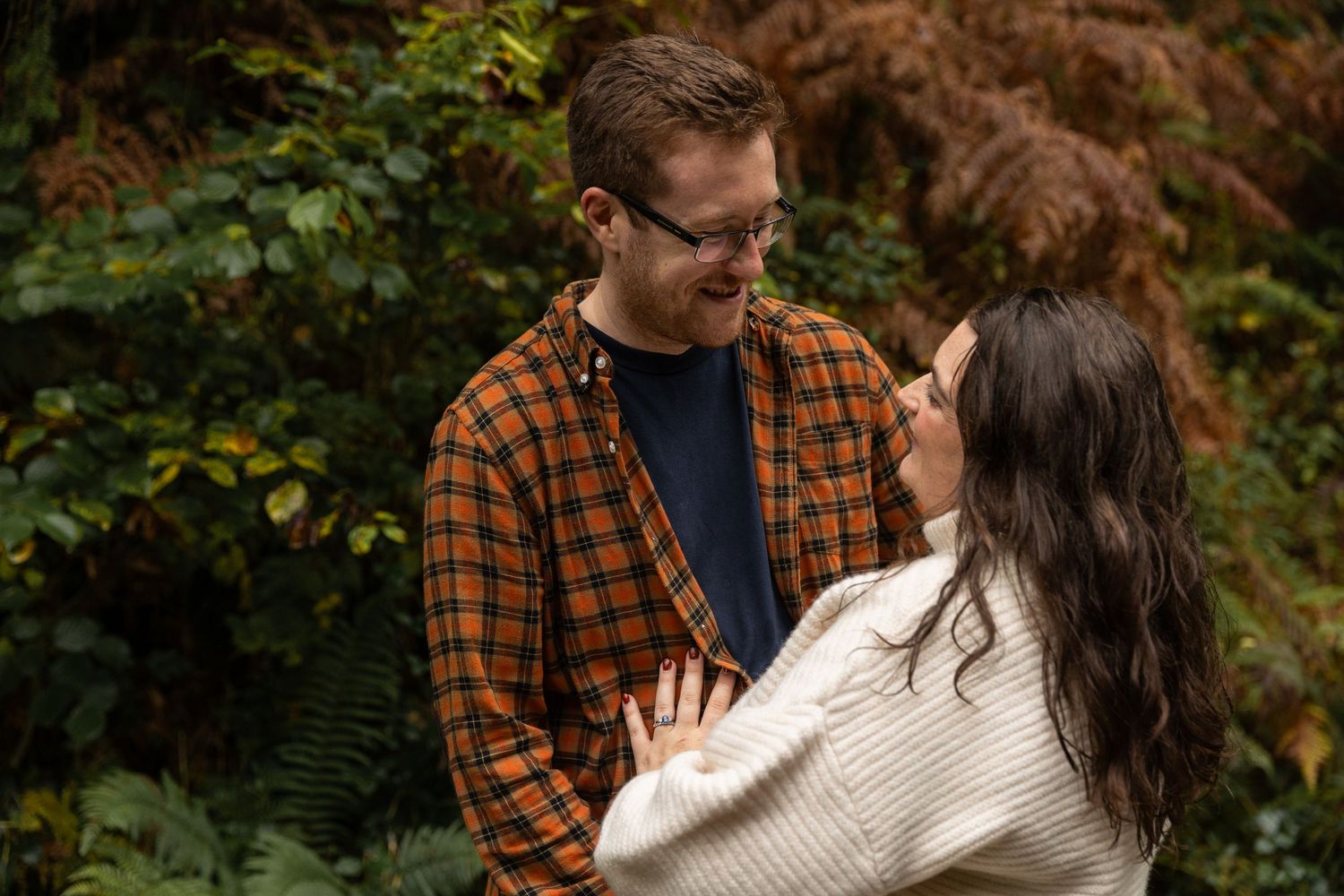 Couple embraces romantically in an autumn forest setting with lush greenery and natural lighting.