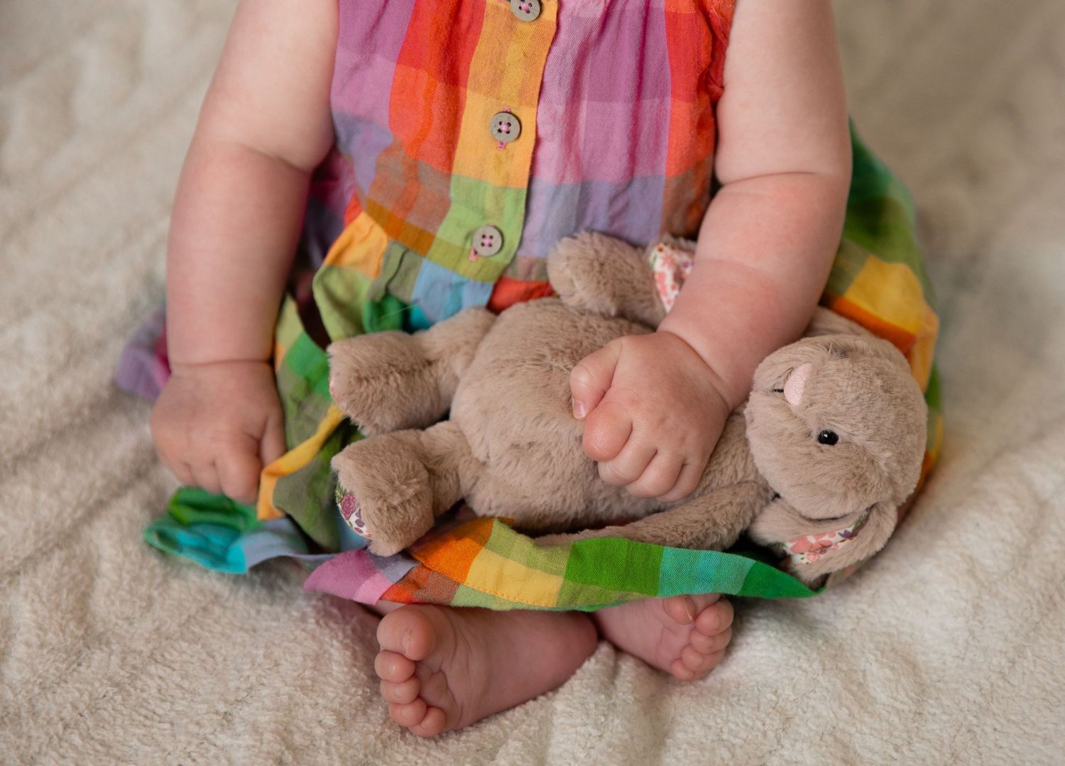 A progression series of baby feet images captured next to a small plush teddy bear toy.