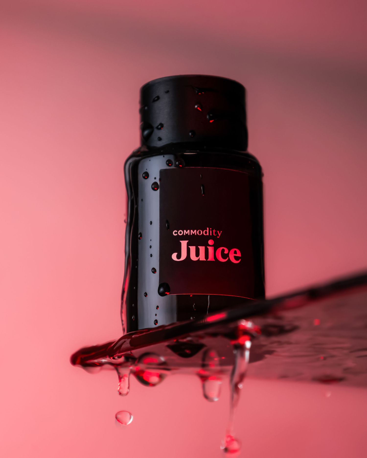 Black Commodity Juice bottle with water droplets against red background.