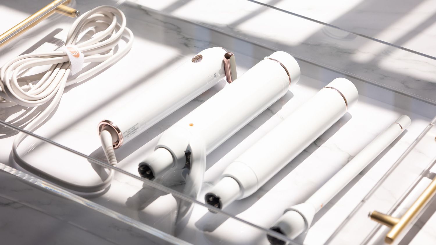 White curling iron wands arranged neatly with cord on reflective surface.