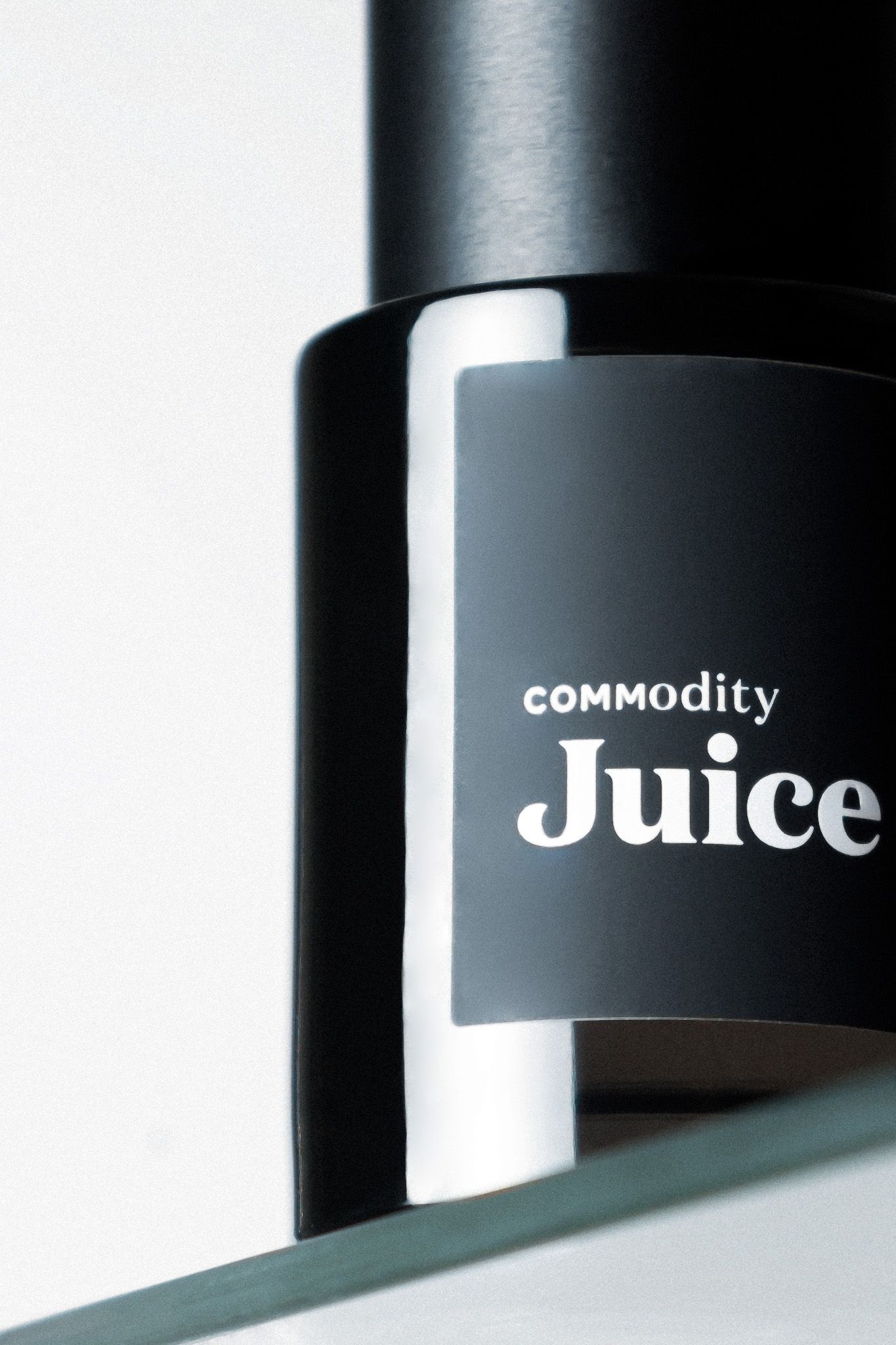 A close-up product shot of a black bottle labeled 'Commodity Juice' with white text against a gradient background.
