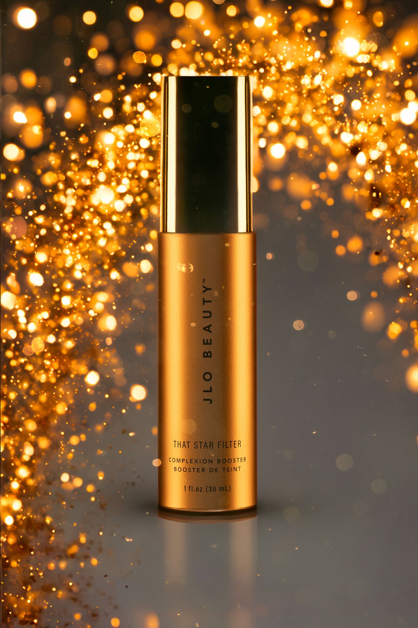 Golden JLO beauty luxury skincare product bottle with glowing bokeh sparkles against dark background.