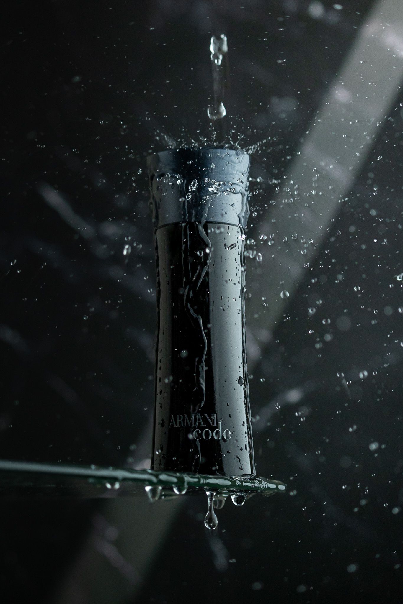 Water droplet splashing on a dark glass bottle against black background with dramatic lighting.